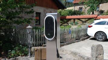 A charging station in a residential area with a stone house, a wooden fence, and a parked car.