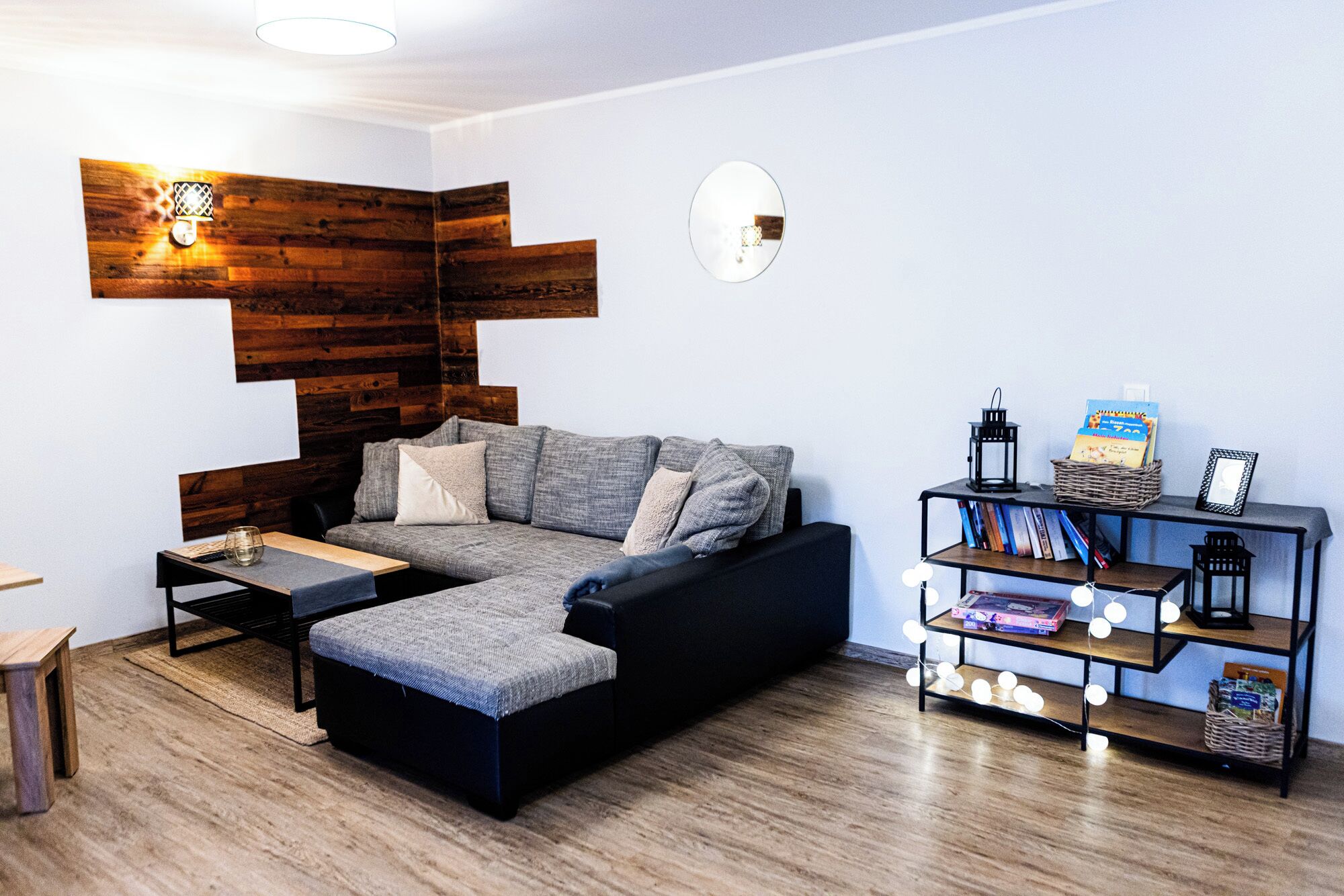 Una sala de estar moderna con un sofá seccional, una mesita de centro, una estantería con libros y objetos decorativos, y una pared de acento de madera.