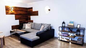 Una sala de estar moderna con un sofá seccional, una mesita de centro, una estantería con libros y objetos decorativos, y una pared de acento de madera.