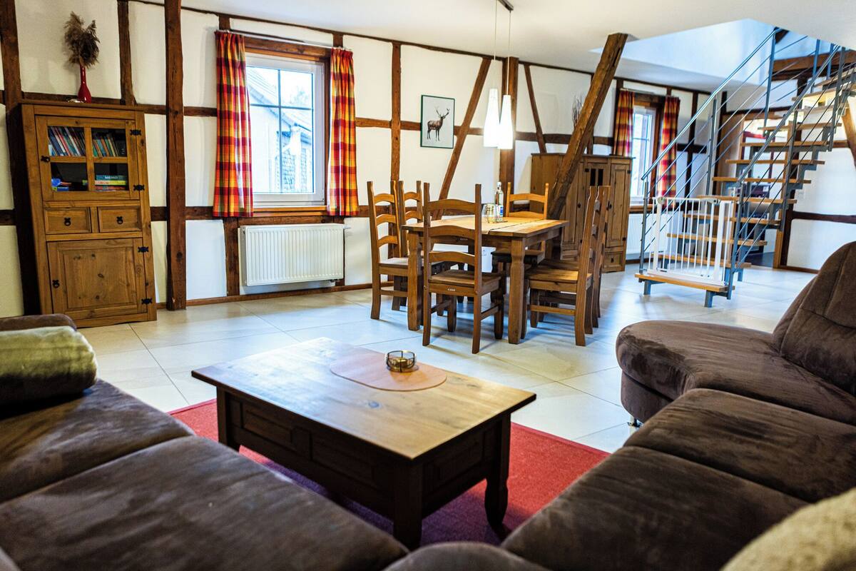A cozy living room with a wooden table, a sofa, and a staircase leading to an upper level.