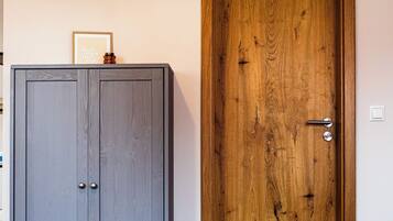 Un dormitorio con una cama, un armario gris, una puerta de madera y un televisor montado.