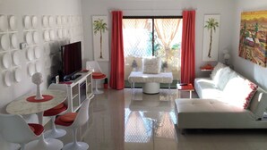 A modern living room with a white sofa, a TV, and a dining area with a table and chairs. - Charming 2-bedroom villa with terrace best view of mountain in Palm Springs area (Cathedral City)