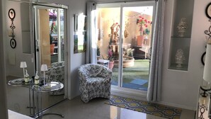 A modern living room with a glass door leading to a patio, a patterned armchair, and a small side table with a lamp. - Charming 2-bedroom villa with terrace best view of mountain in Palm Springs area (Cathedral City)