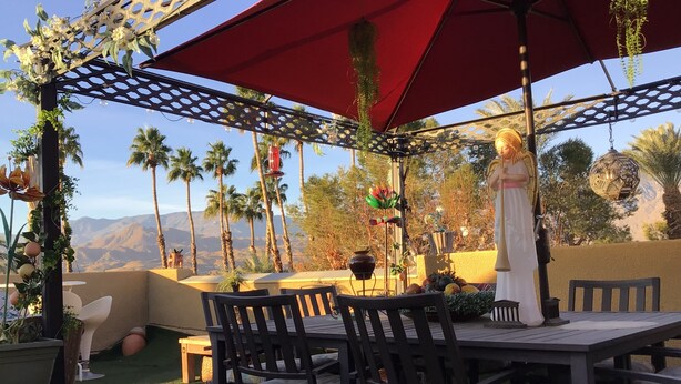 An outdoor patio with a table and chairs, surrounded by decorative plants and a statue. - Charming 2-bedroom villa with terrace best view of mountain in Palm Springs area (Cathedral City)