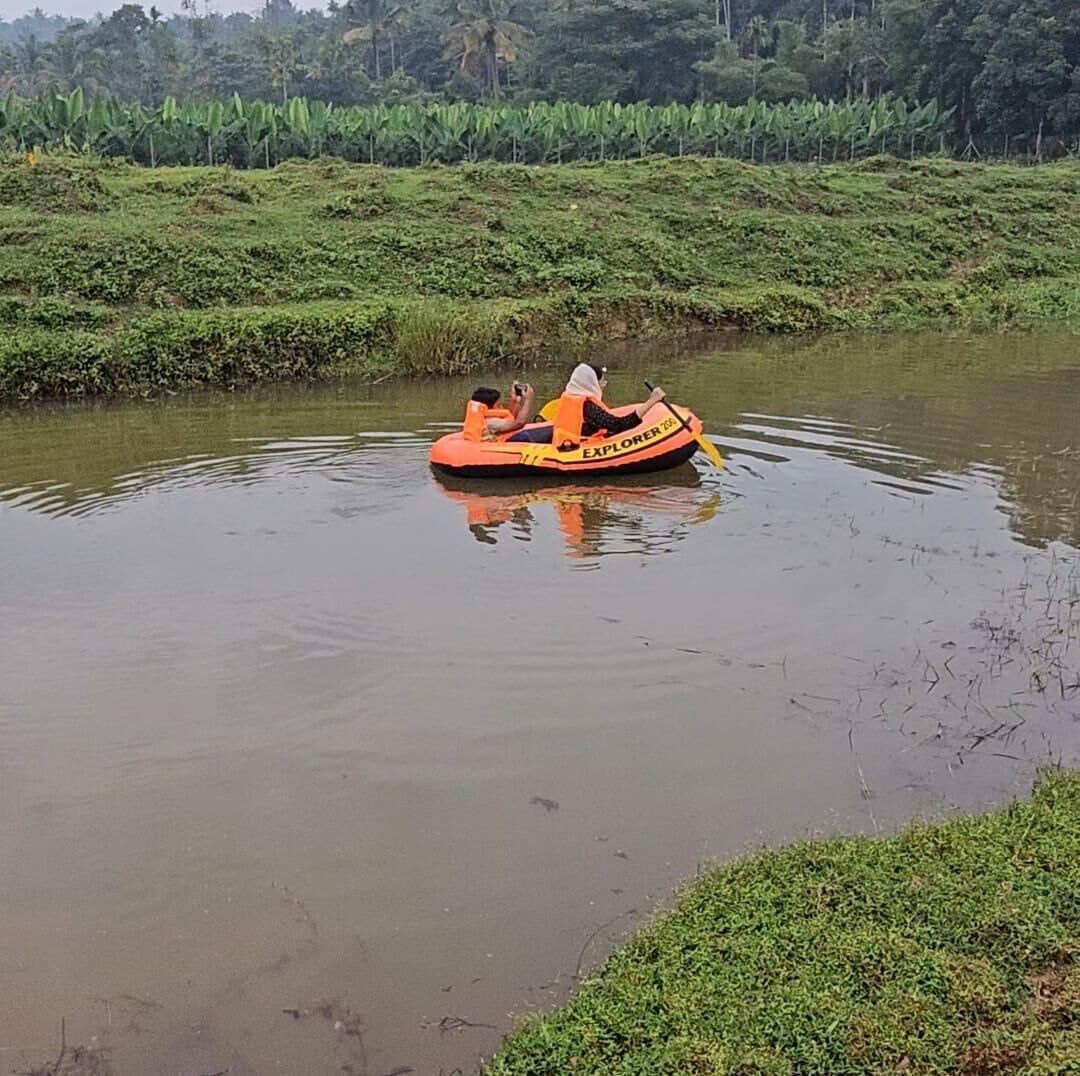 Een persoon in een kleine, oranje opblaasboot op een rustige rivier.
