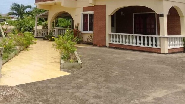 A two-story house with a balcony, a covered porch, and a paved driveway. - Villa Nickerie (Nieuw Nickerie)