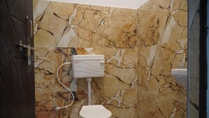 Une salle de bain avec des toilettes, des murs en marbre et un seau rouge.