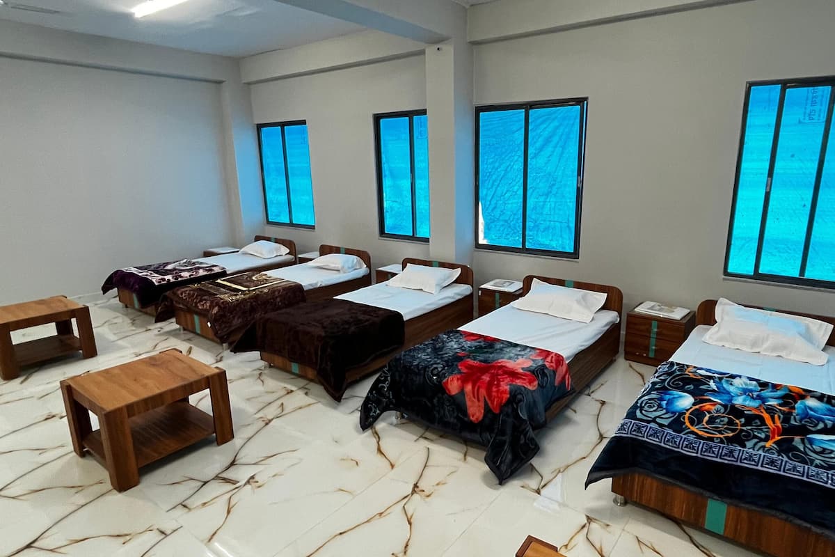 Habitación de hotel con cuatro camas individuales, mesitas de noche de madera y suelo de mármol.