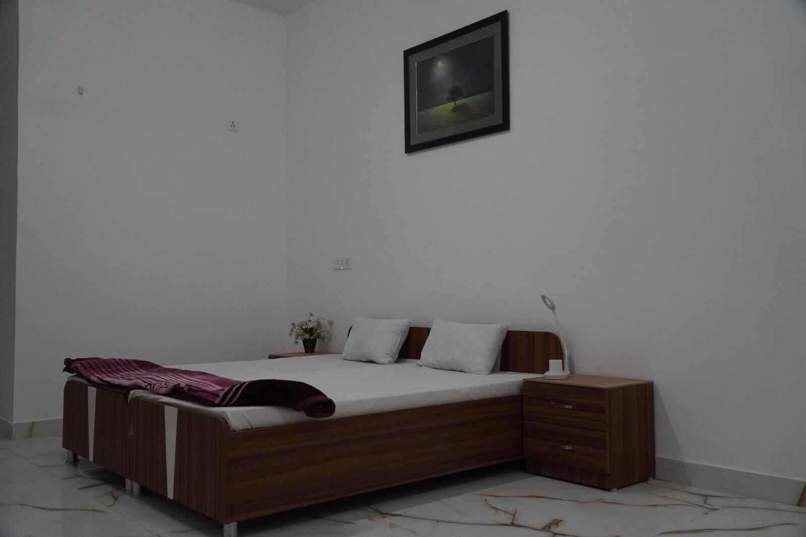 A bedroom with a wooden bed, a nightstand, a bedside lamp, and a framed picture on the wall.
