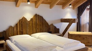 Una cama con estructura de madera y ropa de cama blanca en una habitación con vigas de madera en el techo y cabecera de madera.