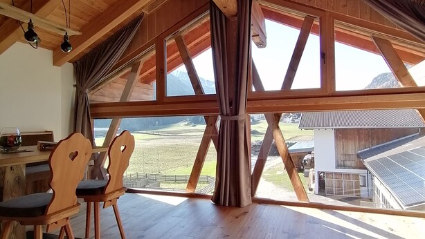 Una habitación amplia con vigas de madera, ventanas grandes y vistas al campo.