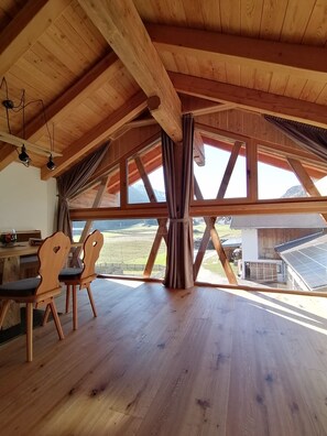 Una habitación amplia con vigas de madera, ventanas grandes y vistas al campo.