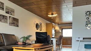 A spacious living room with a wooden ceiling, a black leather sofa, a wooden coffee table, and a patterned rug.