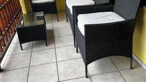 A balcony with wicker furniture, a glass table, and a tiled floor.