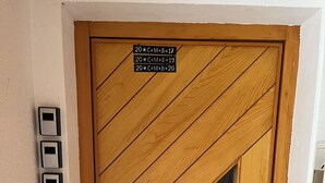 A wooden door with a geometric pattern and a peephole. There are three light switches on the wall to the left of the door.
