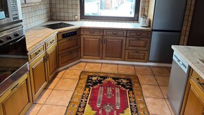 A kitchen with wooden cabinets, a built-in oven, a refrigerator, and a window with curtains.