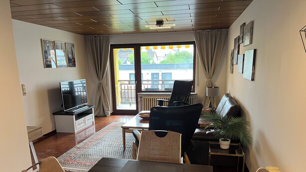 A modern living room with a television, seating area, and a view through the window.