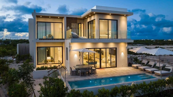 A modern two-story house with a swimming pool, large windows, and outdoor seating. - Waterfront Villa w/ Ocean View, Plunge Pool (Long Bay)