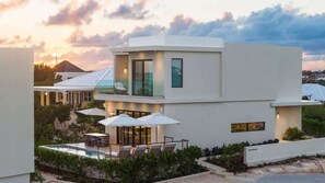 A modern two-story house with a swimming pool, outdoor seating, and a view of the sunset. - Waterfront Villa w/ Ocean View, Plunge Pool (Long Bay)
