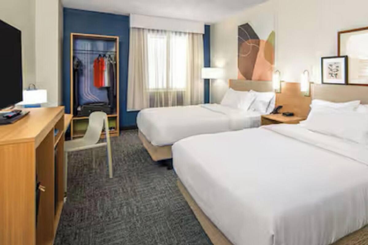 Habitación de hotel con dos camas, un escritorio, una silla, un armario y una ventana con cortinas.