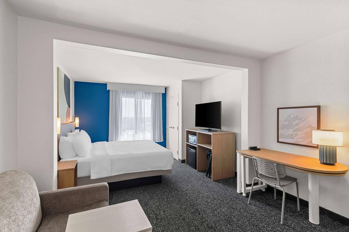 Una habitación de hotel con cama, escritorio, televisor, silla y lámpara.