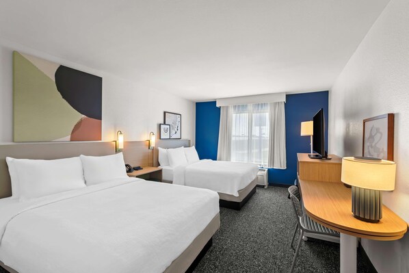 Une chambre d’hôtel avec deux lits, un bureau, une chaise, une lampe et un grand tableau abstrait accroché au mur.