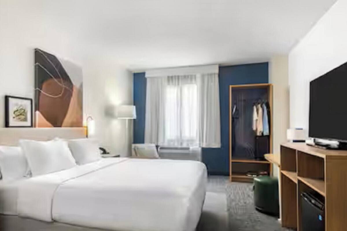 Habitación de hotel con cama, mesitas de noche, televisión, armario y ventana con cortinas.