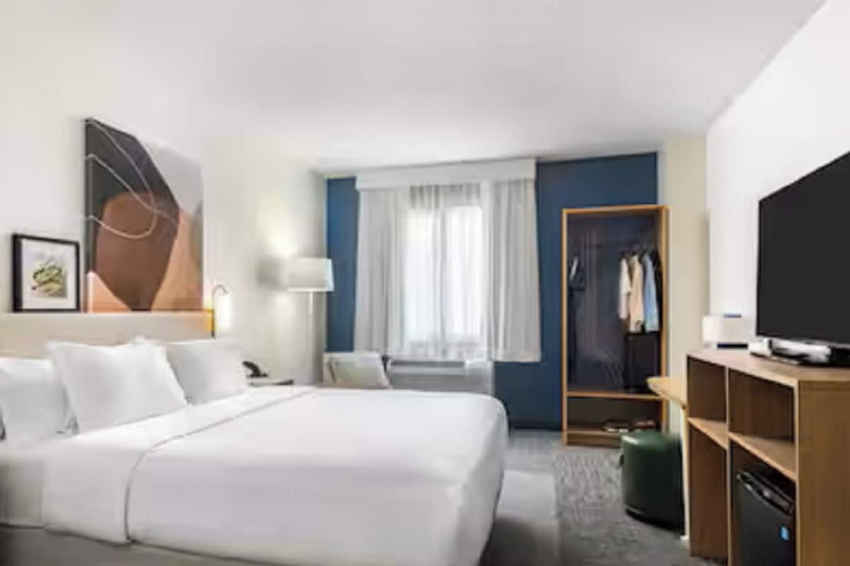 Habitació d'hotel amb un llit gran, taules de nit, un armari, un televisor i una finestra amb cortines.