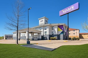 A hotel with a sign reading 'spark by Hilton,' a parking lot, and a building with a modern design.