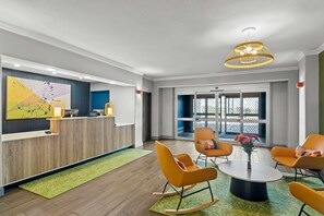 A modern reception area with a wooden reception desk, a large abstract painting, and a seating area with orange chairs and a round table. - Spark by Hilton Killeen (Killeen)