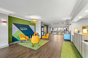 Un hall d’hôtel avec un comptoir d’accueil, des chaises jaune vif, un mur vert orné d’un panneau « Spark » et un plancher en bois.