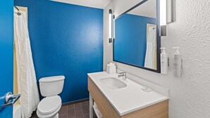 Un bany amb paret blava, vàter blanc i un lavabo amb mirall a la part superior.