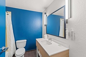 A bathroom with a blue wall, white toilet, and sink with a mirror above. - Spark by Hilton Killeen (Killeen)