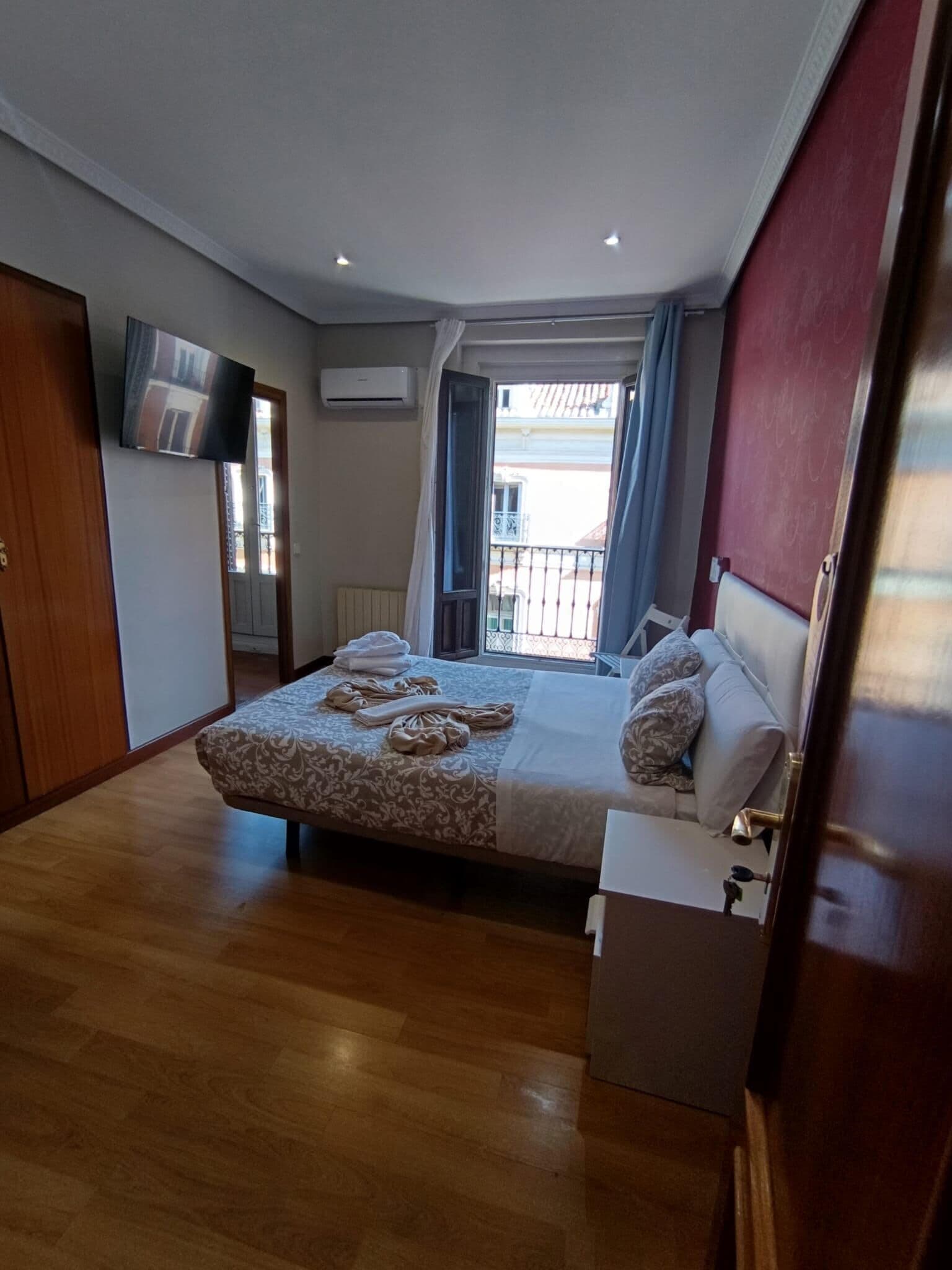 Un dormitorio con cama, mesita de noche, televisor y ventana con cortinas.