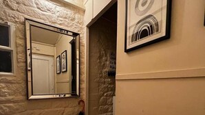 Un couloir avec un mur en pierre, un grand miroir et une œuvre d’art encadrée.