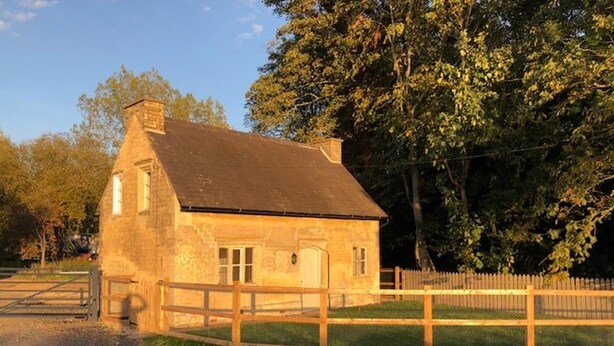 Un bâtiment en pierre avec un toit en pente, une porte en bois et une cour clôturée.