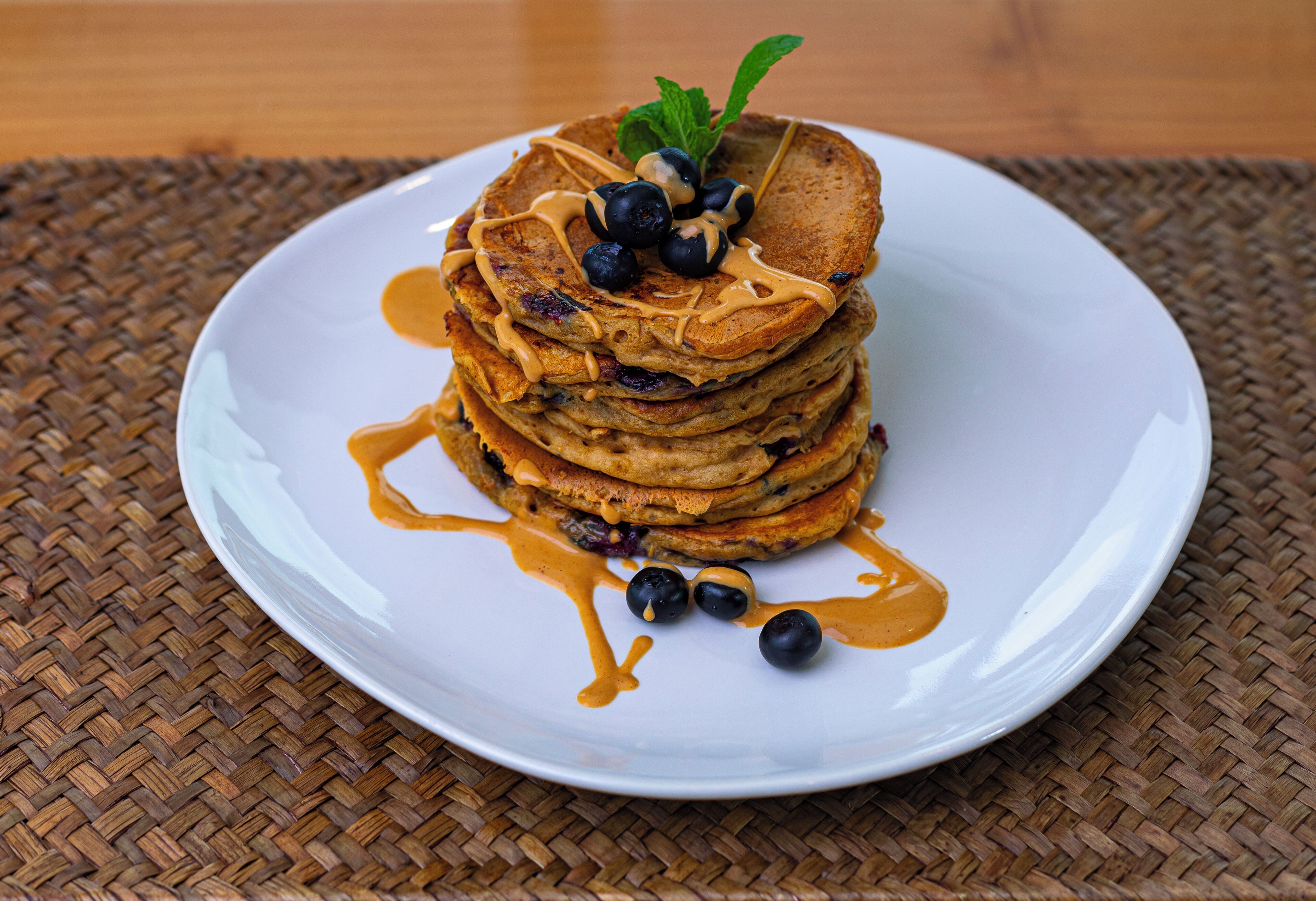 Une pile de crêpes garnies de myrtilles et nappées de sirop, servies sur une assiette blanche.