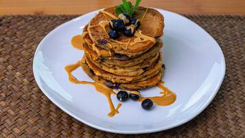 Une pile de crêpes garnies de myrtilles et nappées de sirop, servies sur une assiette blanche.