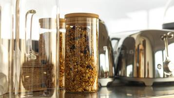 Una encimera de cocina con varios recipientes de vidrio que contienen granos y semillas, un hervidor de acero inoxidable y una jarra de vidrio.