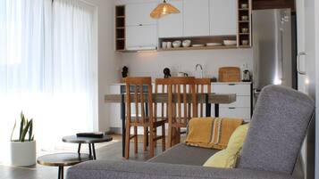 Una sala de estar moderna con un sofá gris, una mesita redonda y un comedor con sillas de madera.