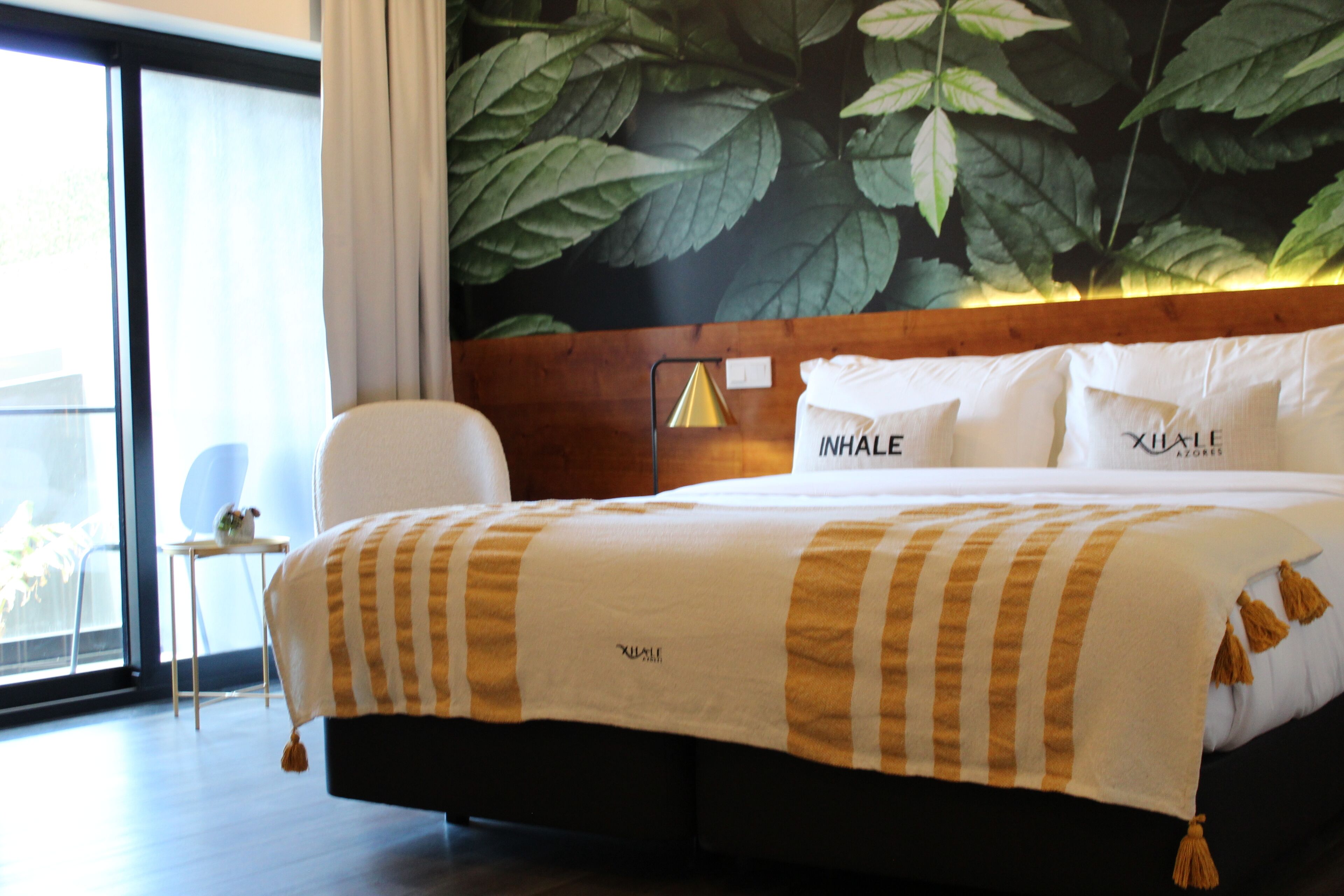 A hotel room with a large bed, a wooden headboard, and a wall mural of leaves.