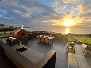 A rooftop patio with a grill, seating, and a view of the sunset over the water. - Xhale Azores (Angra do Heroismo)