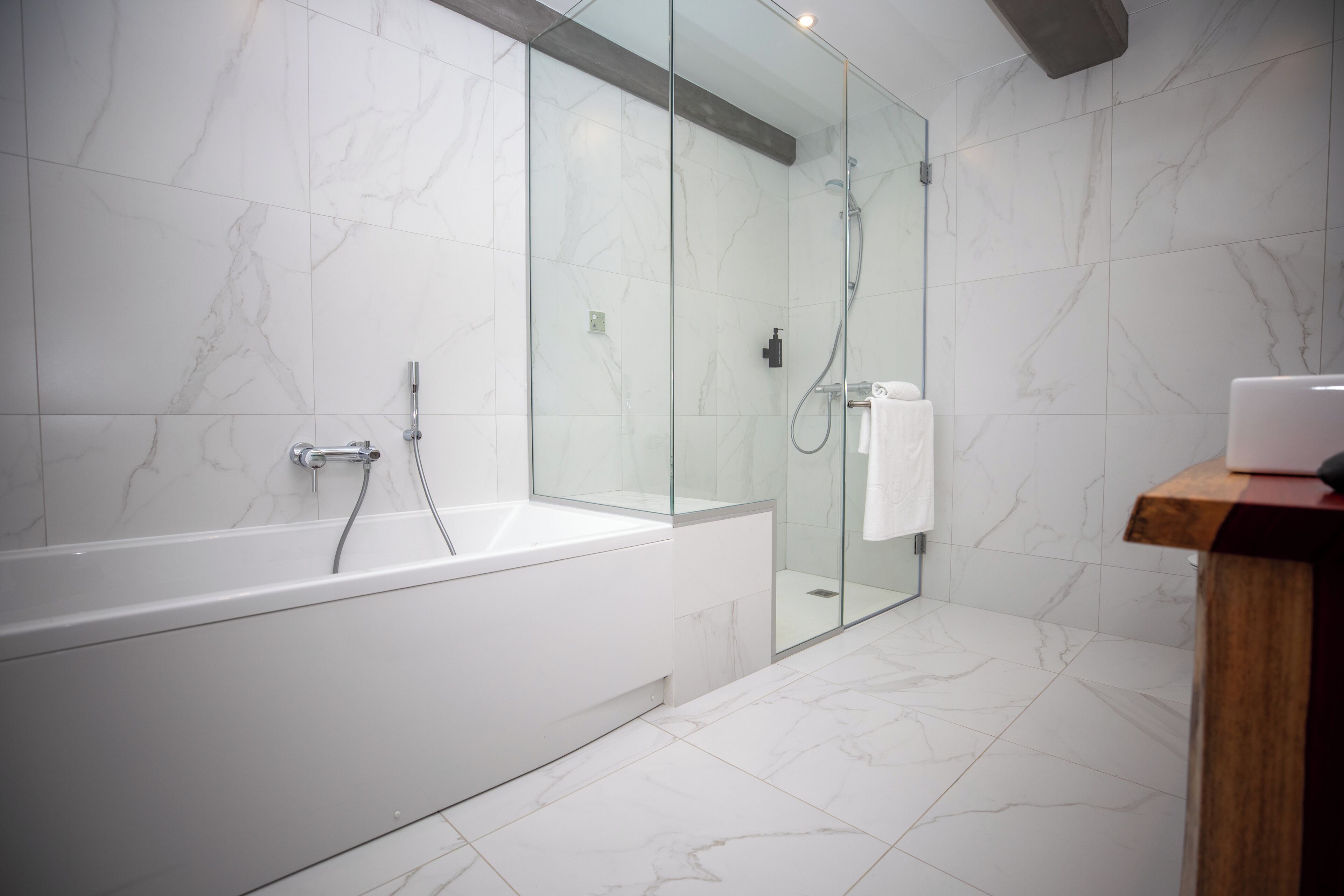 Ein modernes Badezimmer mit einer gläsernen Duschkabine, einer weißen Badewanne und einem hölzernen Waschtisch.