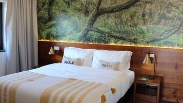Habitación de hotel con cama, mesita de noche, lámpara y un mural en la pared con temática forestal.