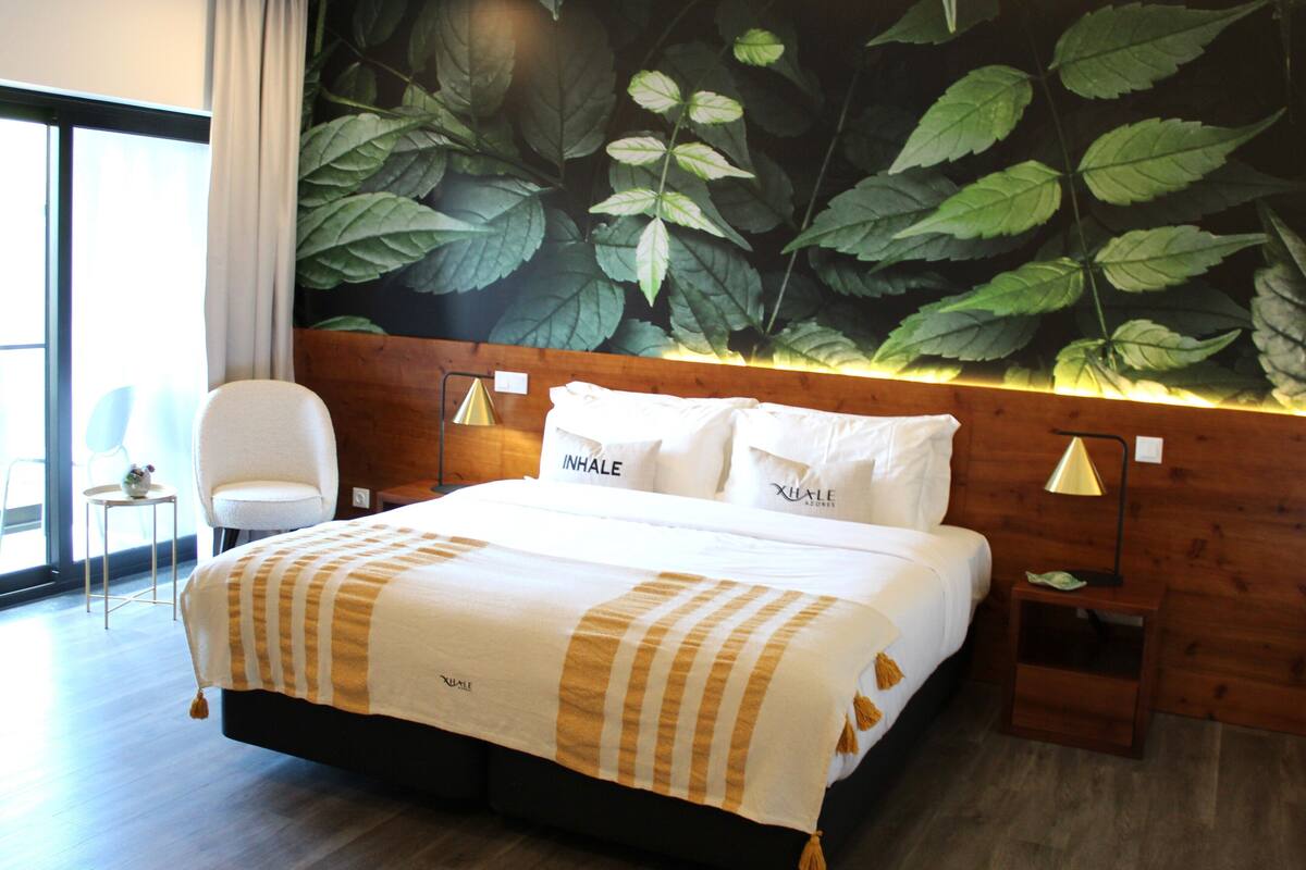 A hotel room with a large bed, a wooden headboard, and a wall mural of leaves.
