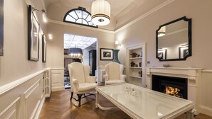 Un salon spacieux avec une cheminée, une table basse en verre et deux fauteuils en cuir blanc.