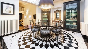 Un coin repas avec un sol à carreaux noirs et blancs, une table ronde entourée de chaises et un lustre.