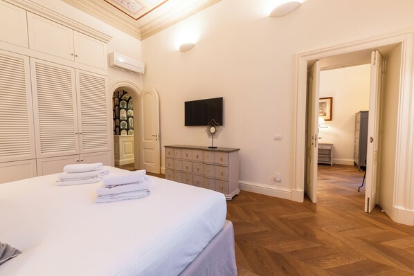 A bedroom with a bed, a dresser, a television, and a hallway leading to another room. - Rinascimento Privato by MMega (Florence)