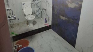 Een badkamer met een marmeren vloer, een toilet, een douche en een blauwe emmer.