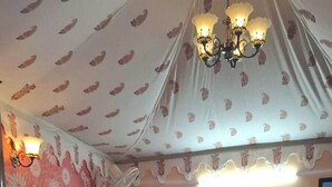 Een slaapkamer met een bed, een behang met patroon, een kroonluchter en een deur.